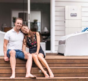 Image showing a husband and wife embracing with a Redback Technologies Smart Battery Installed on the porch behind htem