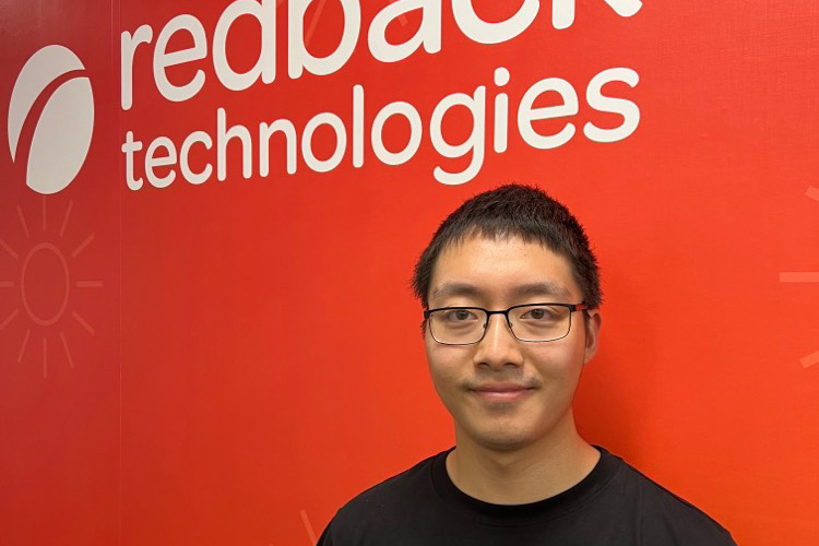 A person wearing glasses in front of the Redback Technologies logo on a wall.