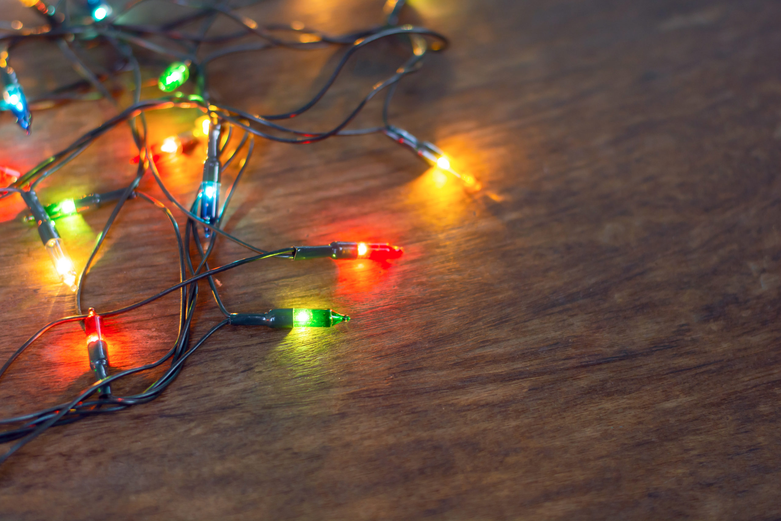 Colourful Christmas lights over dark wooden background, flat lay.