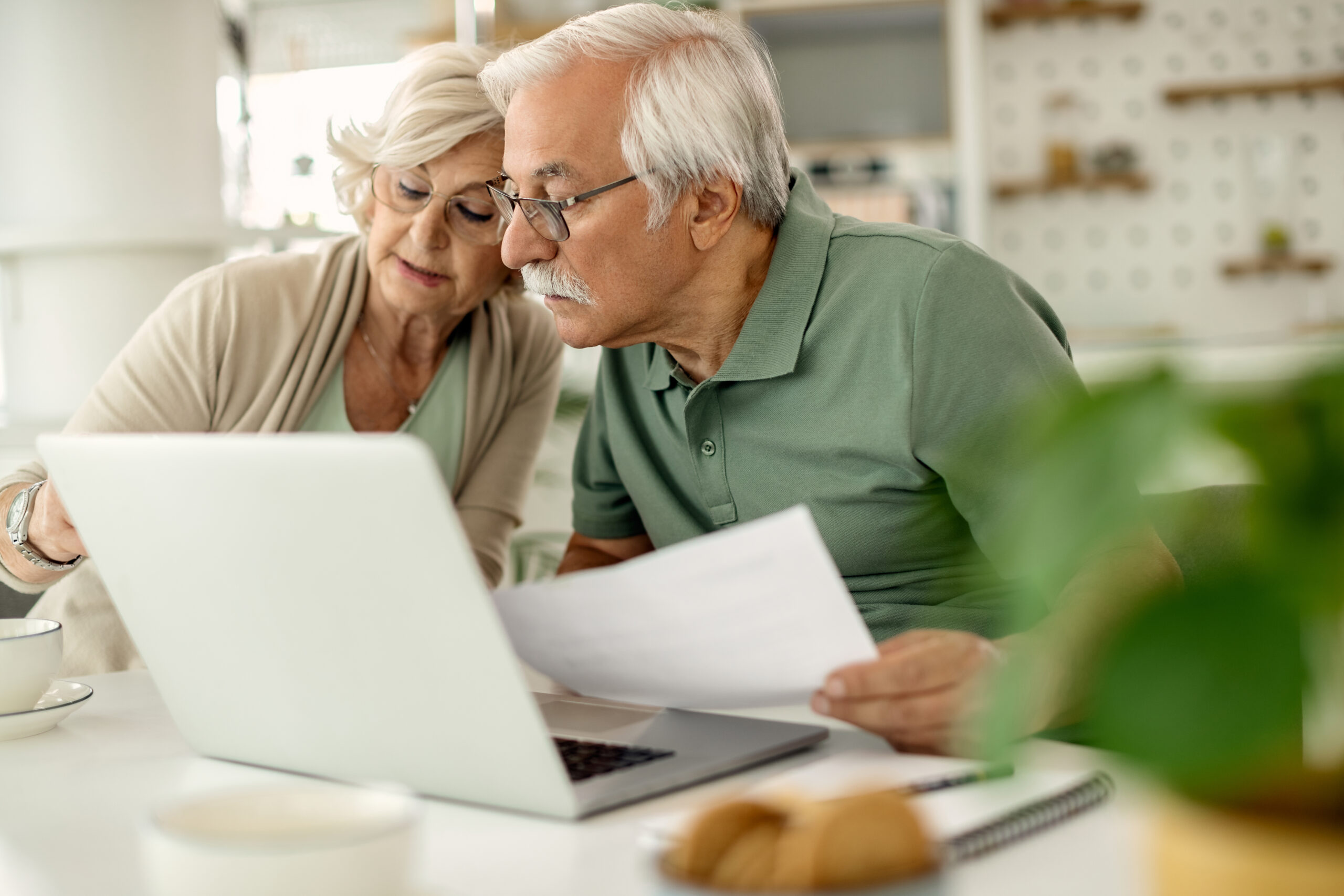 A senior couple is using a laptop while analysing documents together